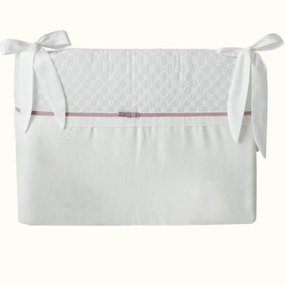 Protetor de berço bege e branco com laços e detalhe rosa, delicado para enxoval de bebê.