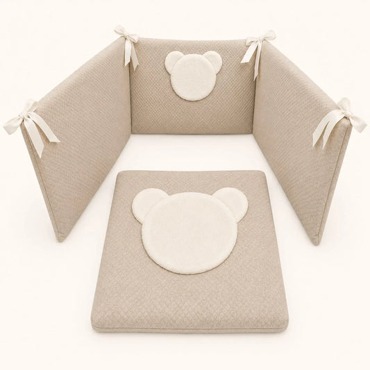 Conjunto de berço com protetores e colchão em tons neutros, com detalhes de urso fofo e laços