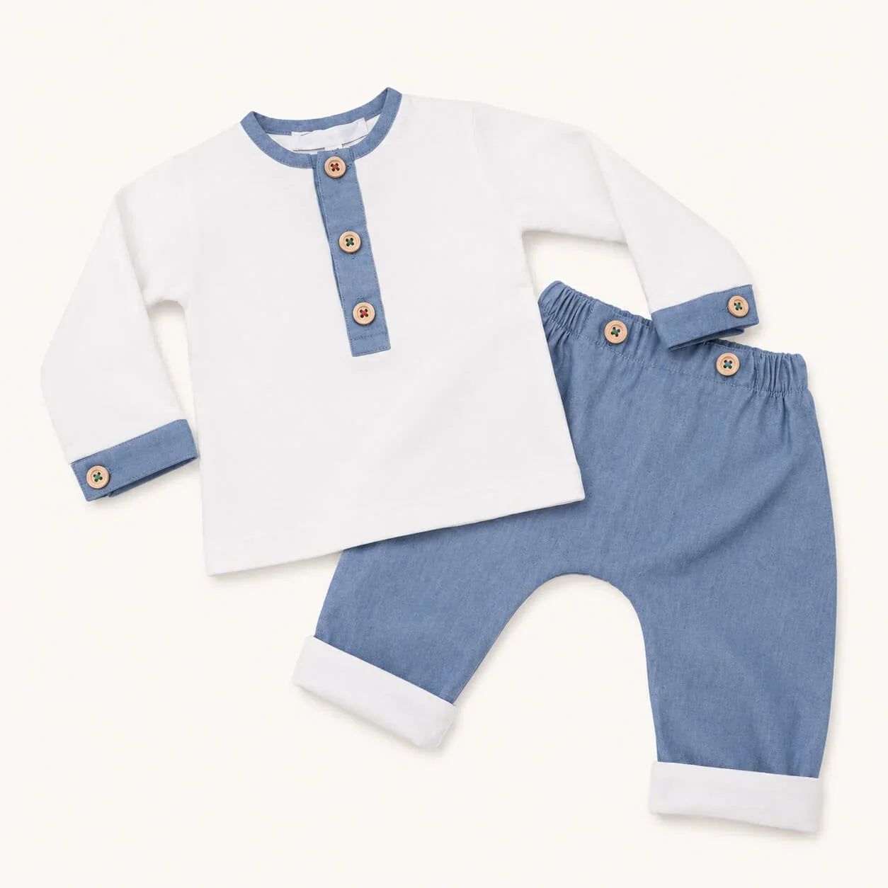 Conjunto de roupa de bebé em algodão, com camisola branca e calças azuis, botões decorativos e acabamentos em contraste.
