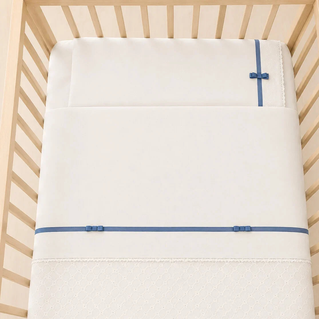 Berço com lençóis romantic bege com fita e laços azul, composto por lençol de cima, lençol capa e fronha. Popeline 100% algodão com tratamento anti-pilling.