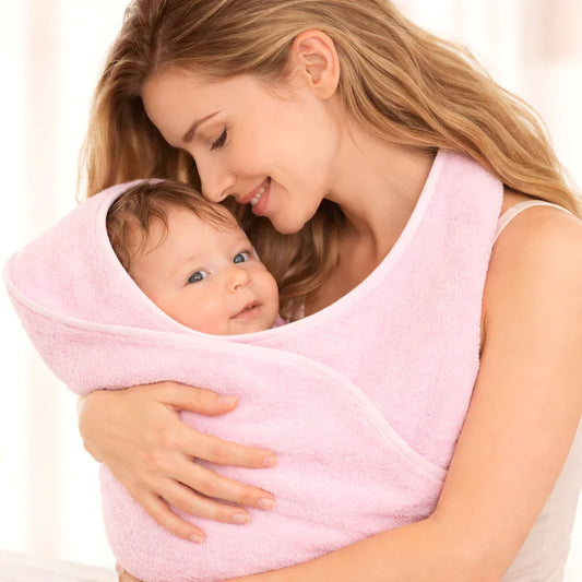 Mãe abraça bebê enrolado em toalha rosa macia, roupa de banho confortável para recém-nascidos.