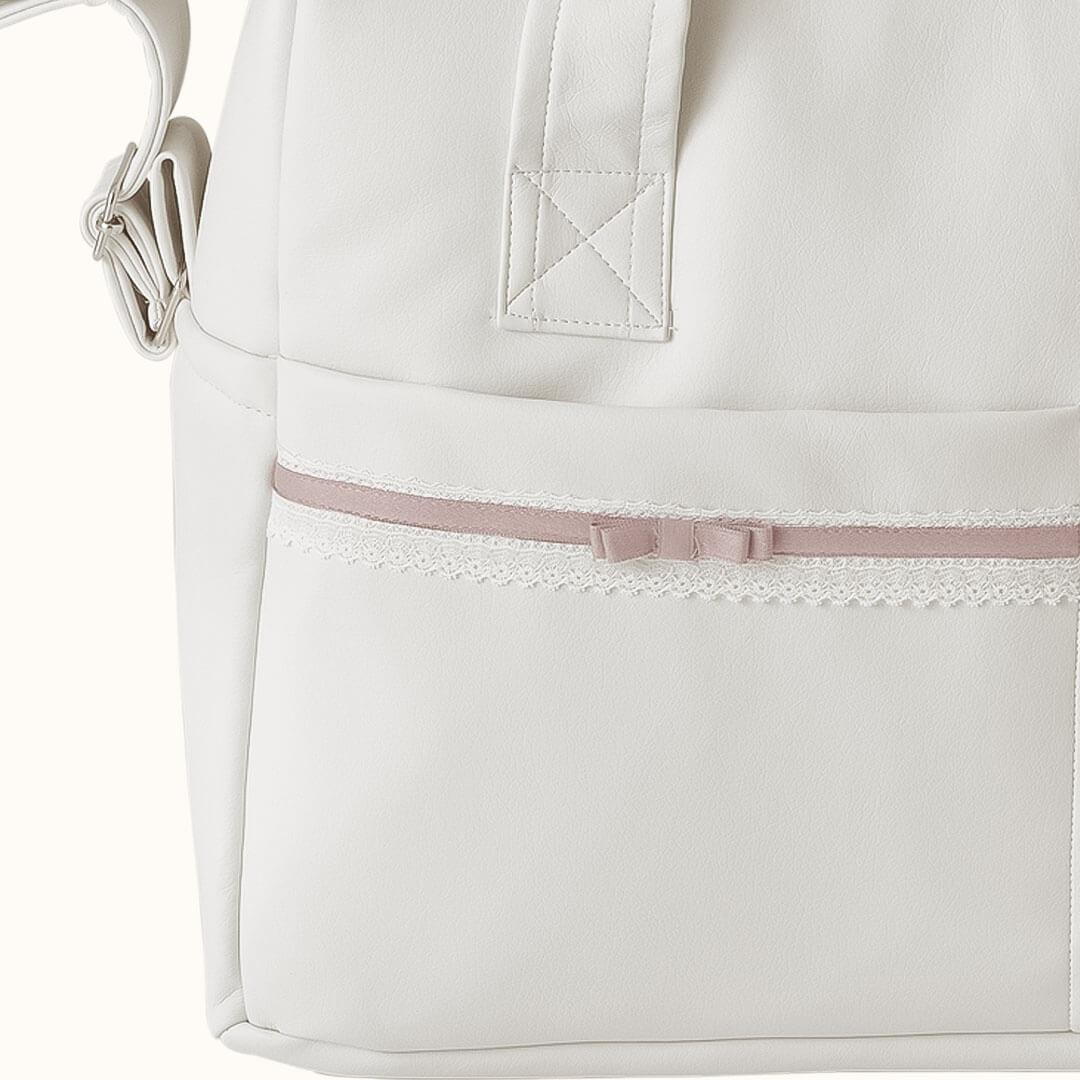 Detalhe de mala maternidade bege claro com fita rosa e renda, ideal para enxoval de bebé.