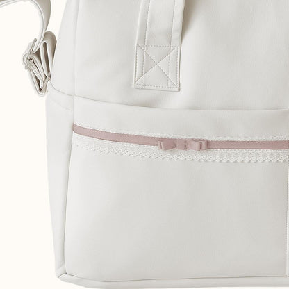 Detalhe de mala maternidade bege claro com fita rosa e renda, ideal para enxoval de bebé.
