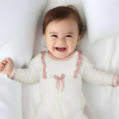 bebê sorrindo deitado, vestindo macacão branco com detalhes rosa, roupa confortável para recém-nascido