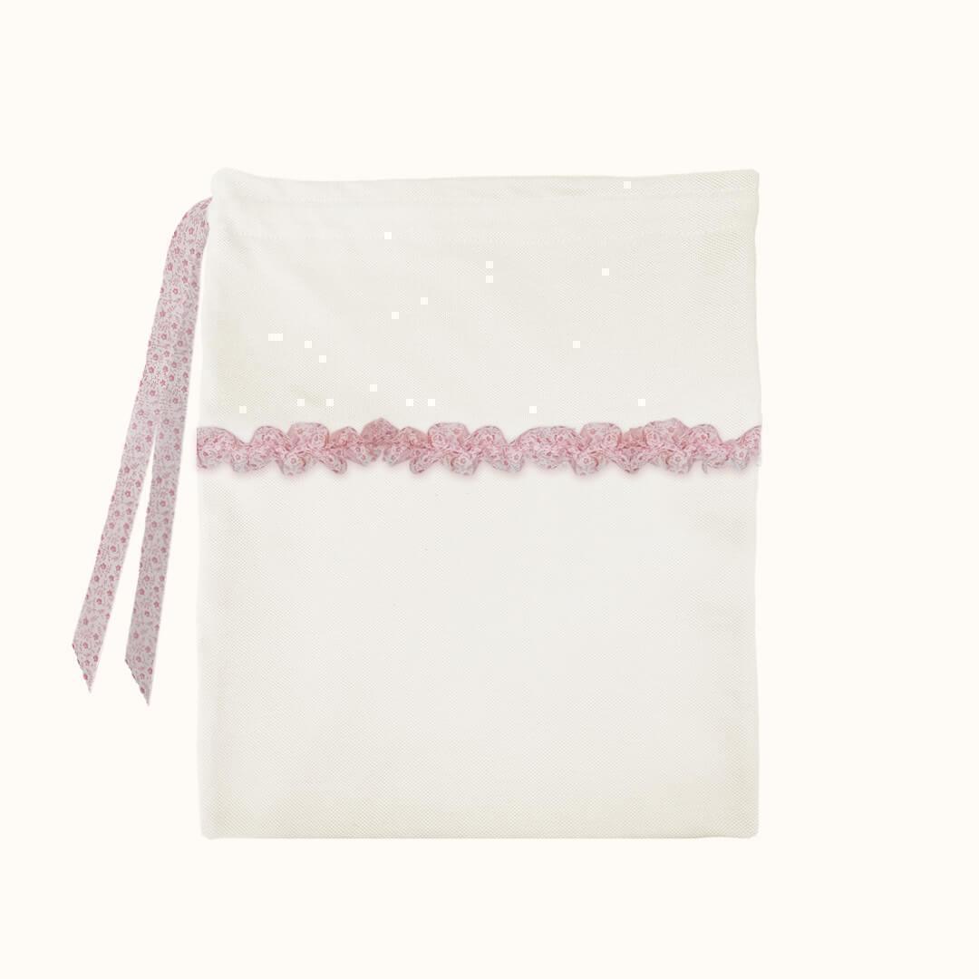Saco de tecido branco para bebé com laço e detalhe de renda rosa, fundo neutro