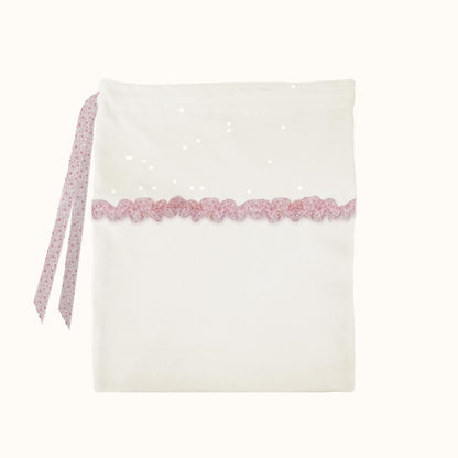 Saco de tecido branco para bebé com laço e detalhe de renda rosa, fundo neutro