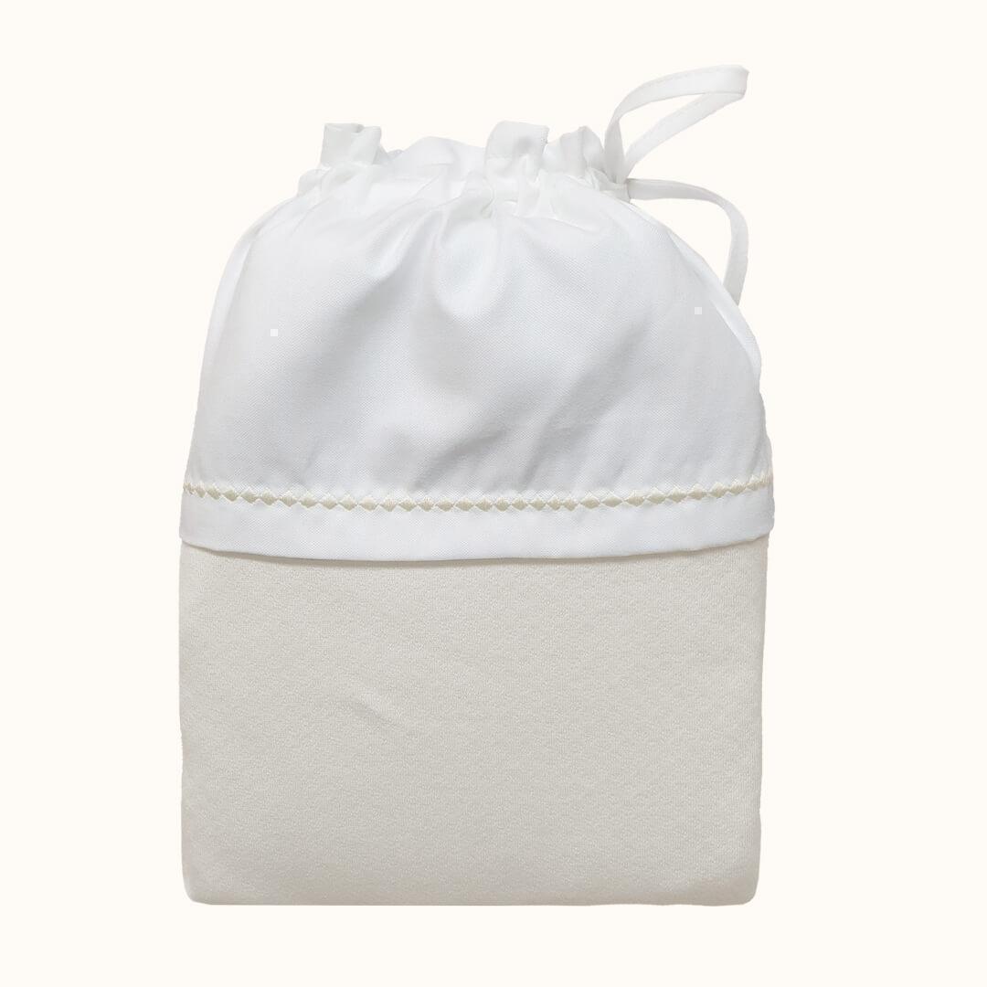 Saco de bebé bege e branco em tecido macio com fecho de cordão, ideal para enxoval de recém-nascido.