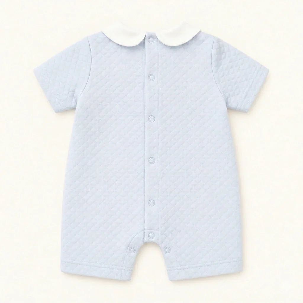 Macacão de bebê azul claro matelassê com gola branca e botões frontais, roupa confortável para recém-nascido.