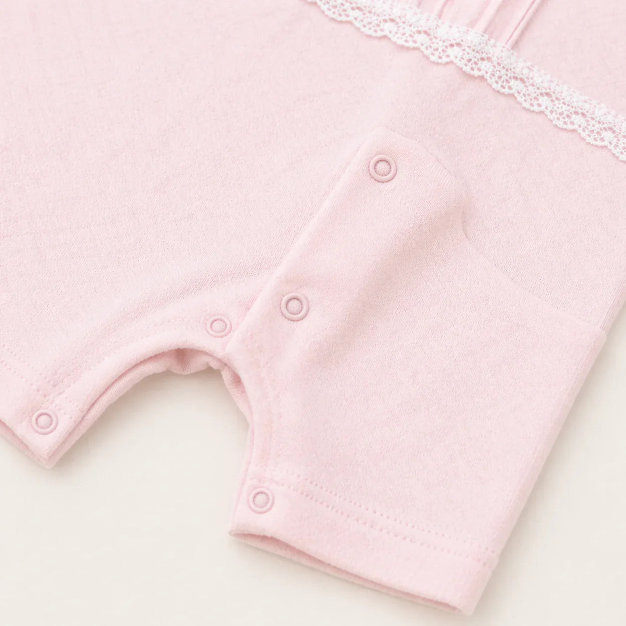 Detalhe de macacão de bebê rosa com botões de pressão e renda, roupa confortável para recém-nascido
