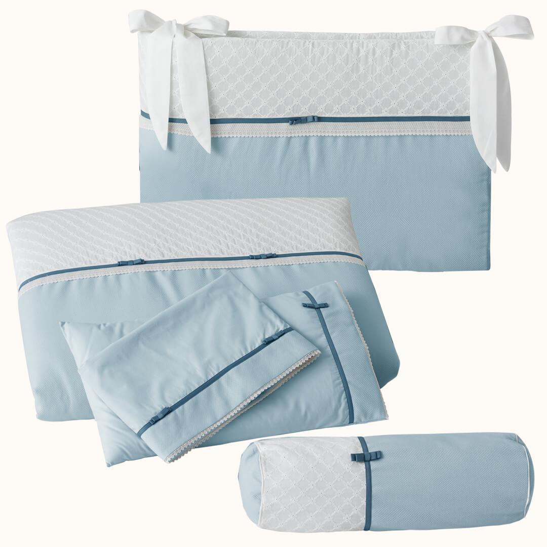 Conjunto de roupa de berço azul com almofada, edredom, protetor e detalhes rendados.