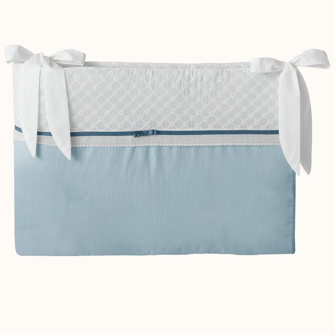 Protetor de berço azul e branco com laços, detalhes em renda e acabamento delicado.