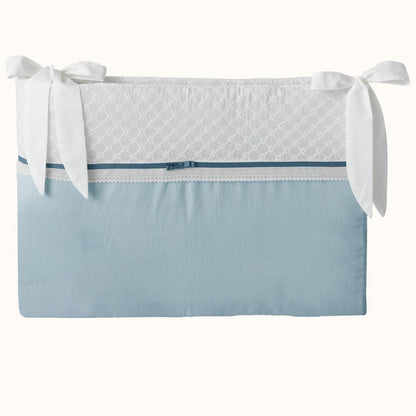 Protetor de berço azul e branco com laços, detalhes em renda e acabamento delicado.