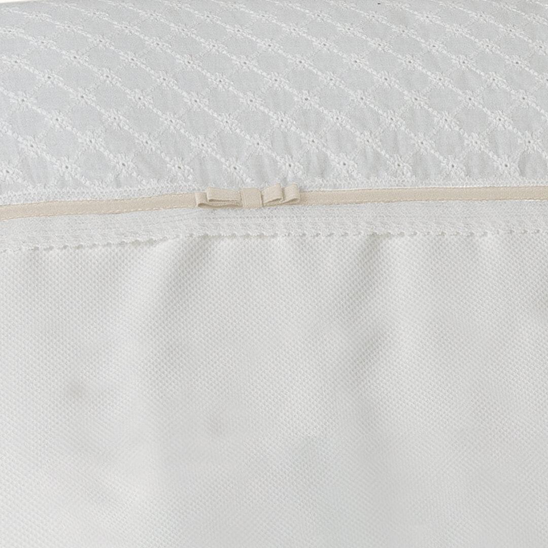 Detalhe de roupa de berço bege e pérola com laço e bordado delicado para bebê