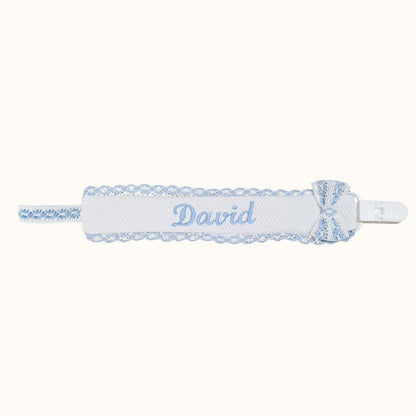 Suporte de chupeta branco com detalhes em azul, laço e nome bordado, acessório para bebé.