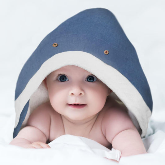Bebê sorrindo enrolado em toalha de banho com capuz azul e branco, enxoval confortável.